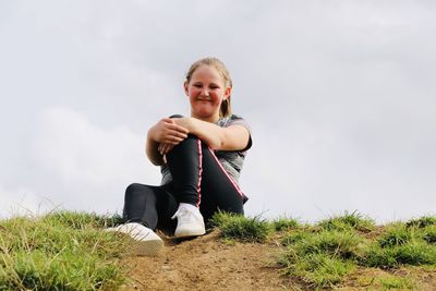 Portrait of smiling girl sitting on land against sky