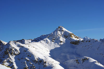 Low angle view of snowcapped mountains against clear blue sky