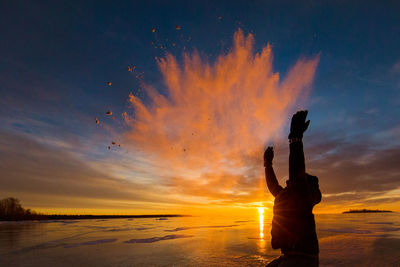 Silhouette man with arms raised at beach against cloudy sky during sunset