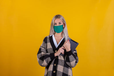 Portrait of woman wearing mask with digital tablet against yellow background