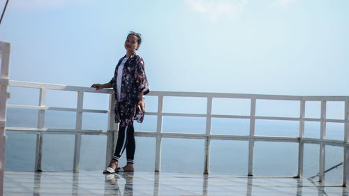 Full length of young man standing on railing against sea