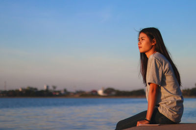 Side view of woman sitting against sky during sunset