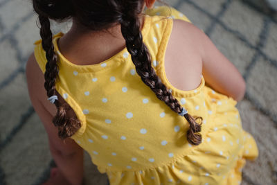 Little girl with braids in yellow dress from behind