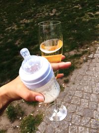 Cropped hand of woman holding baby bottle and champagne glass on footpath