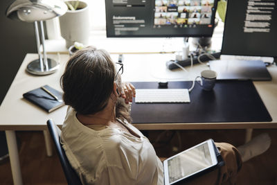 High angle view of freelancer sitting with tablet pc at desk in home office