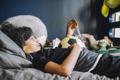 Girl looking at medal while lying on bed in bedroom