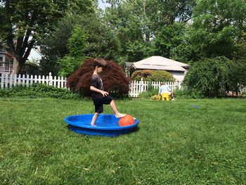 Side view of boy playing with ball in small wading pool at lawn
