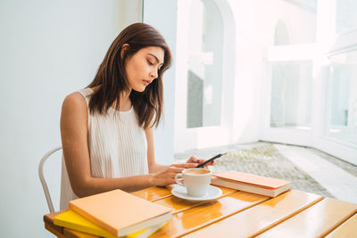 Young woman using phone while sitting on table