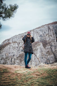 Woman looking through binoculars while standing on rock against sky