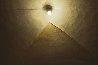 Low angle view of illuminated light bulb against wall