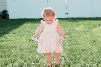 Cute girl holding sandals while walking on grass at backyard