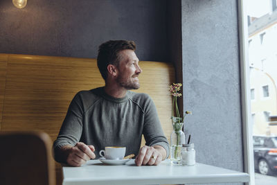 Smiling mature man sitting in cafe looking out of window