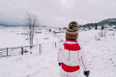 Rear view of woman standing on snow covered field against sky