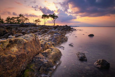 Rocks on shore against sky during sunset