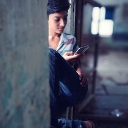 Teenage boy using mobile phone while sitting on window sill