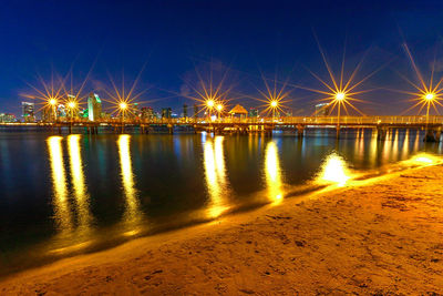 Illuminated street lights by river against sky at night