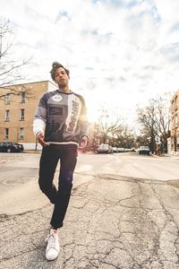 Full length portrait of young man standing against sky in city