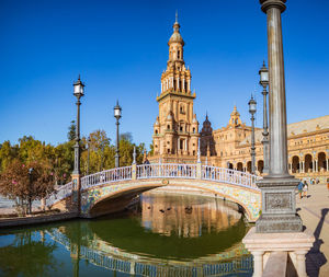 Arch bridge over canal in city against clear blue sky