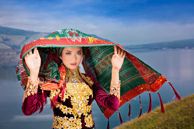 Portrait of woman in traditional clothing standing against lake and sky