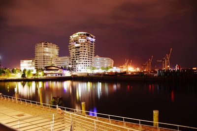 Illuminated buildings by river against sky at night