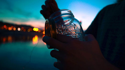 Close-up of hand holding illuminated water against sea at night