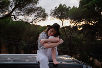 Portrait of young woman standing by tree against plants