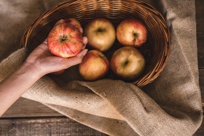 Cropped hand of woman holding apples in basket on table