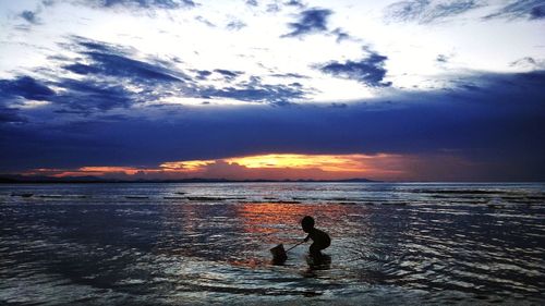 Silhouette boy on beach against sky during sunset