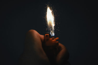 Cropped hand holding illuminated cigarette lighter against black background