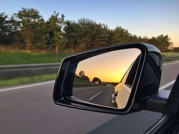 Road reflecting on side-view mirror of car during sunset