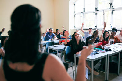 Students raising hands to answer questions asked by teacher in classroom