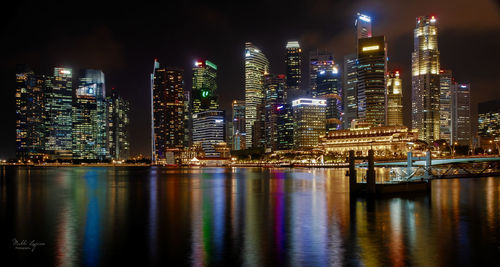 Illuminated city by river against sky at night