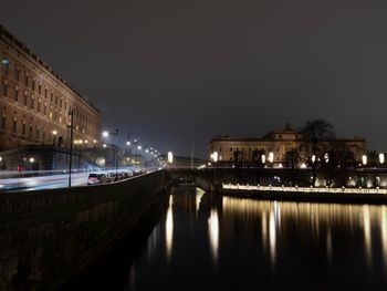 Illuminated buildings by river against sky at night