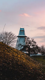 Bare trees by building against sky during sunset