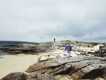 Rear view of child walking on rocky beach against sky