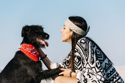 Side view of woman playing with dog against clear sky