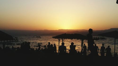 Silhouette people on beach against clear sky during sunset