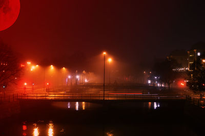 Illuminated bridge over river against sky at night