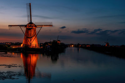 Cranes in illuminated city against sky at sunset