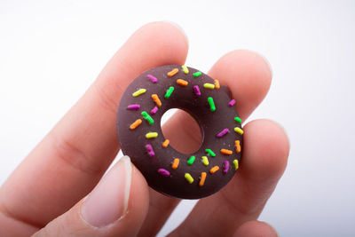 Cropped hand of woman holding donut against white background