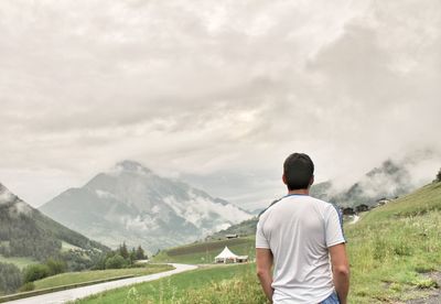 Rear view of man standing on grass against mountains and sky