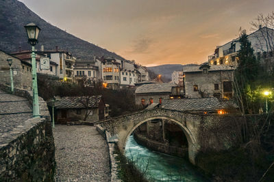 Bridge over river amidst buildings against sky at dusk