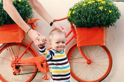 Portrait of cute boy in mother arms in front of a orange bycicle