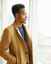 Mid adult man looking away while standing against window