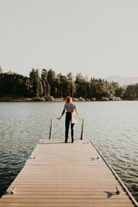 Man standing on pier over lake against clear sky