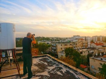 Man photographing cityscape against sky during sunset