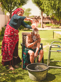 Daughter bathing her old mother in yard