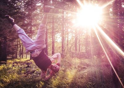 Man doing handstand against sunlight streaming through trees in forest