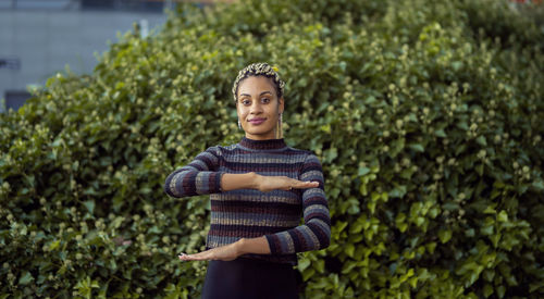 Portrait of woman gesturing while standing against plants