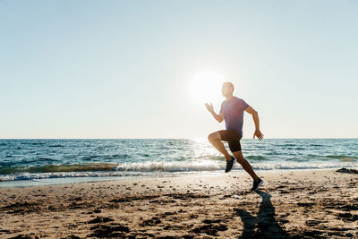 Man running on beach against clear sky